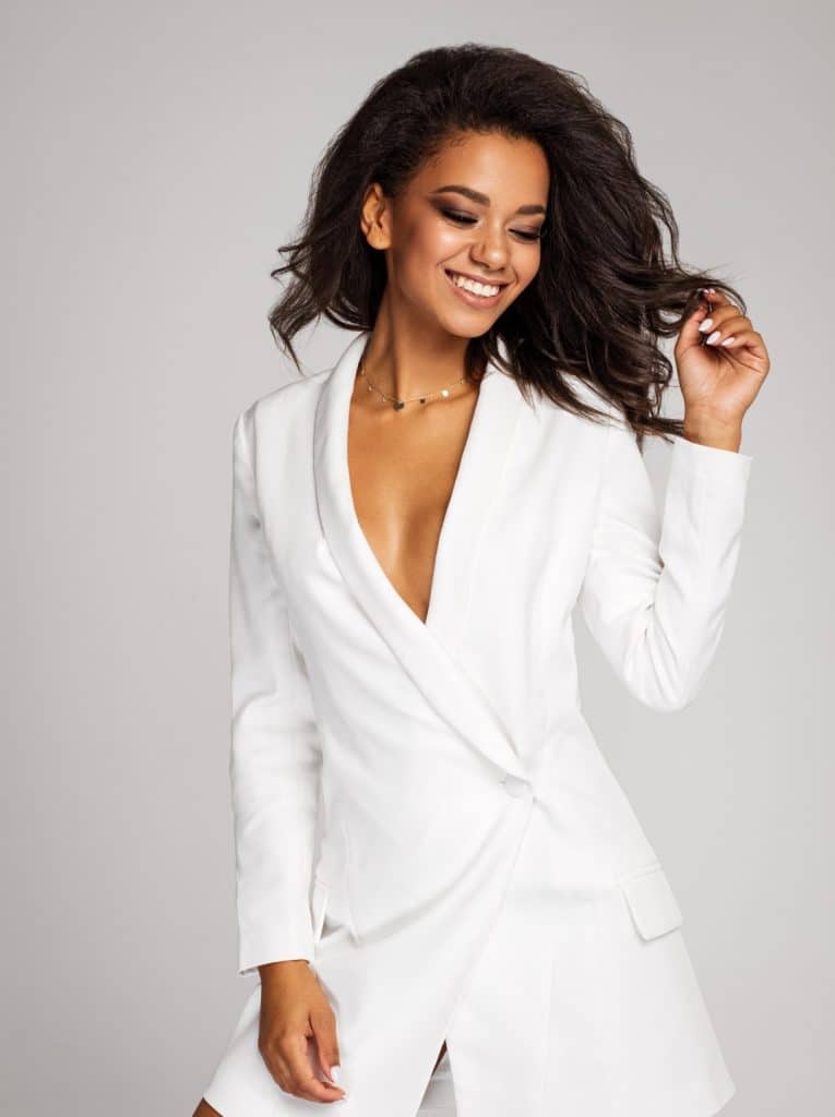Beautiful woman in a white suit stands with one hand touching her hair and one touching her thigh to model hair stimulation services on the homepage of ILEA Hair Restoration.