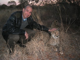 Photo of Dr. Cesar petting a cheetah and showing off his shaved head with noticeable hair loss.