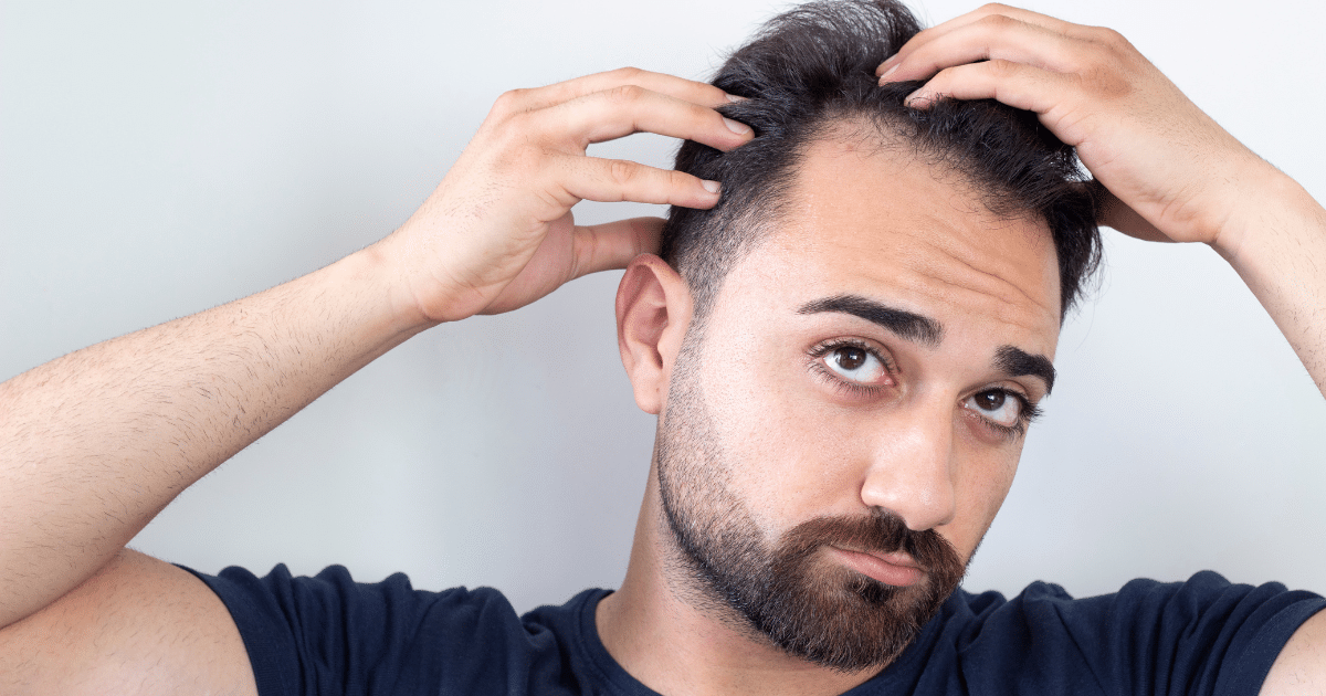 Image of a man looking worried while examining his hair.